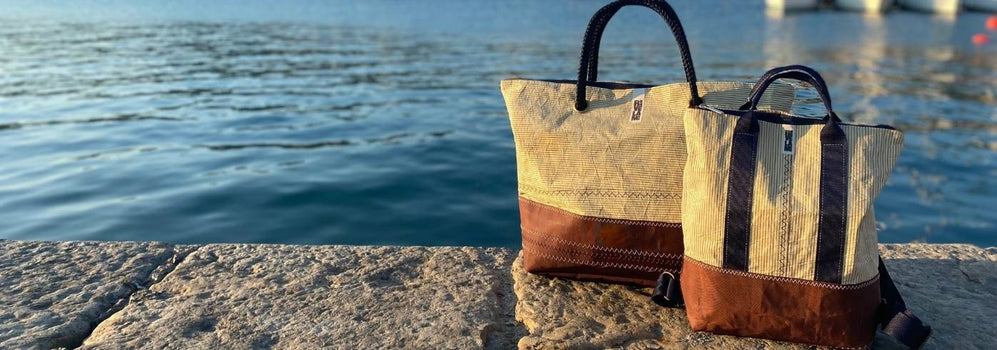 borsa grande e zaino fatte con vele color beige appoggiate a terra su pontile davanti al mare