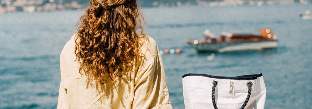 donna di spalle che guarda il lago difianco borsa bianca