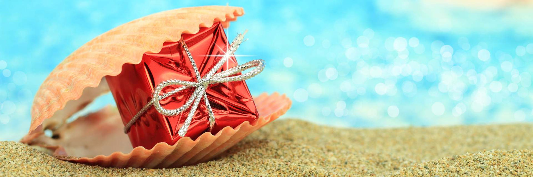 pacchetto regalo rosso inserito in una conchiglia sulla sabbia